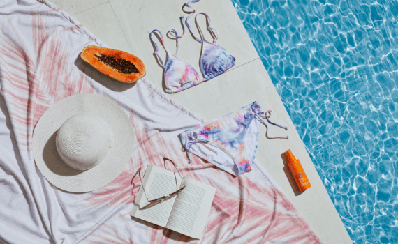 Een hoed, boek, zonnebrand, fruit en een bikini liggend aan de rand van het zwembad